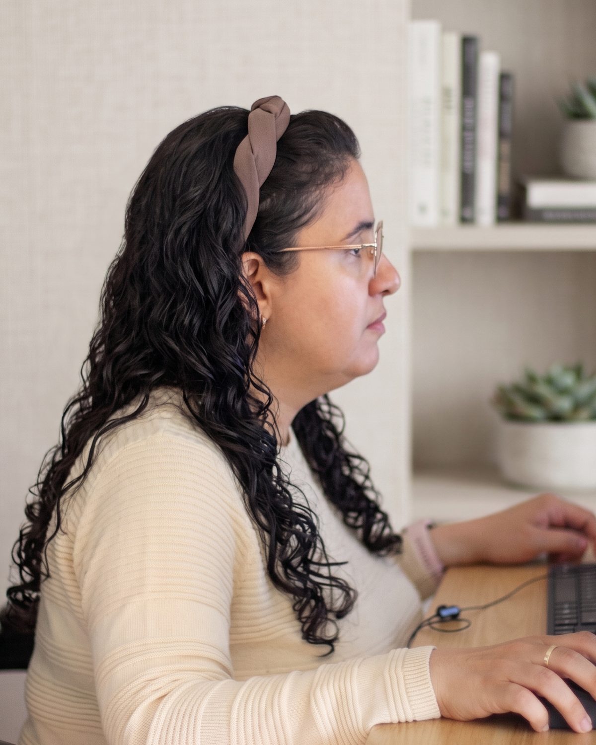 Oriana Zambrano working at her desk, seen in profile, one hand on the keyboard and one on the mouse, looking at the screen.